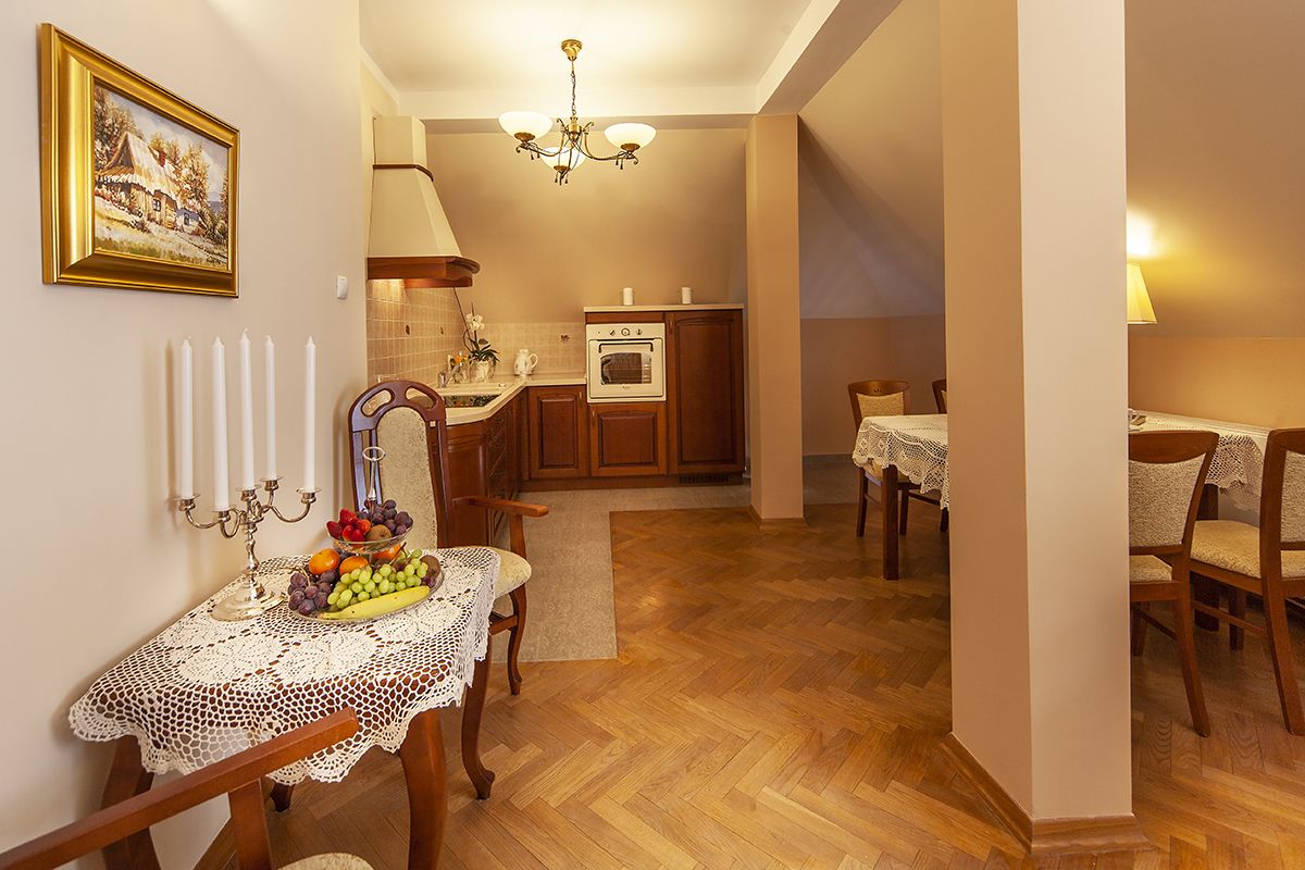 A cozy dining area with a table set for two, a chandelier, and a kitchen in the background.