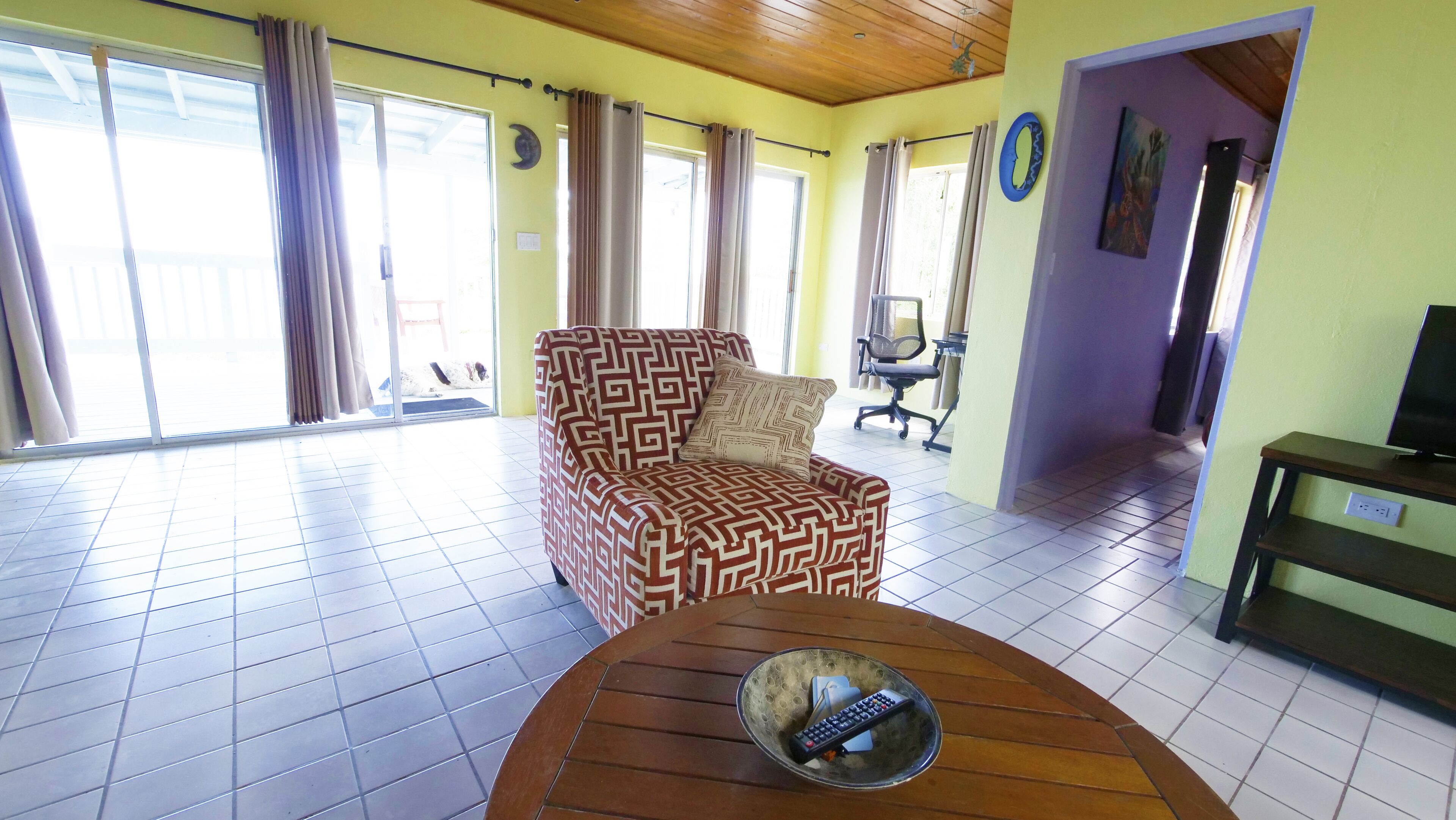 A living room with a patterned sofa, a coffee table with a remote control, and a TV stand.