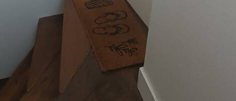Un couloir étroit doté d’un plancher en bois, d’une porte blanche et d’une petite boîte en carton ornée de symboles.