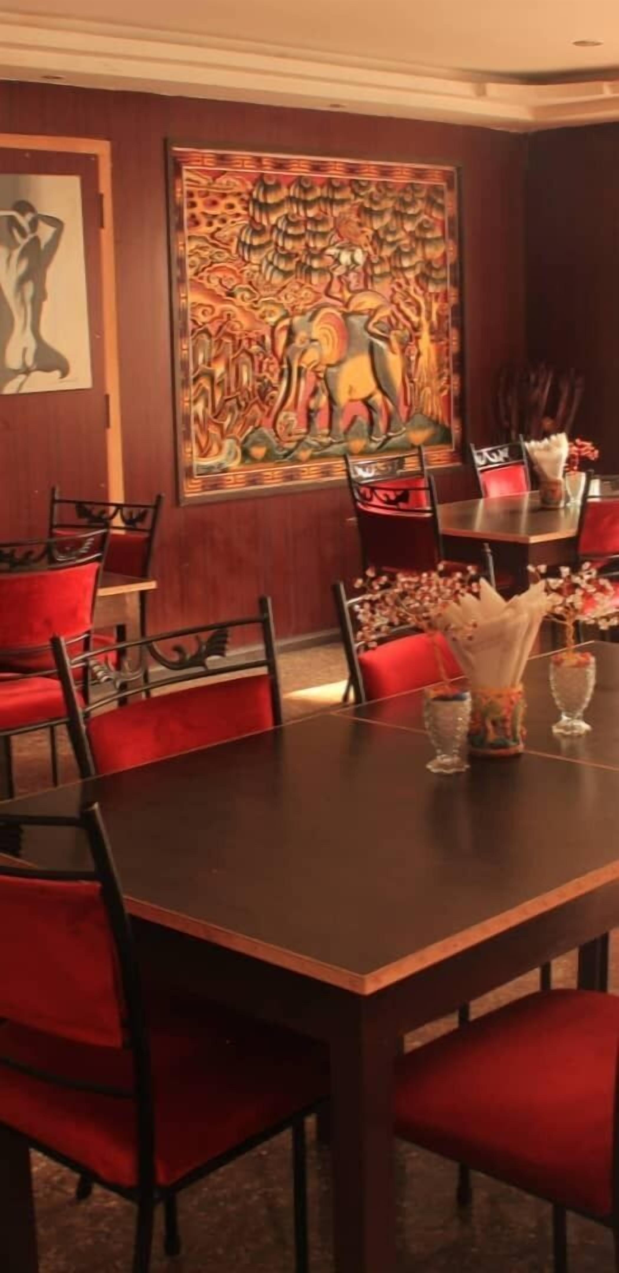 A dining area with a dark wooden table, red upholstered chairs, and a large decorative painting on the wall.