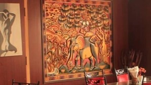 Un comedor con una mesa de madera oscura, sillas tapizadas rojas y un cuadro decorativo grande en la pared.