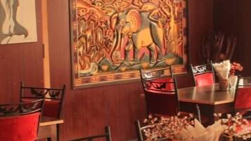 A dining area with a dark wooden table, red upholstered chairs, and a large decorative painting on the wall.