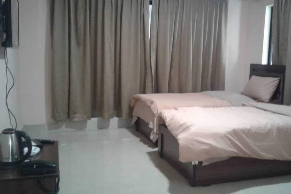 A hotel room with two single beds, a wooden headboard, a coffee maker, and a view of the outside through the window.