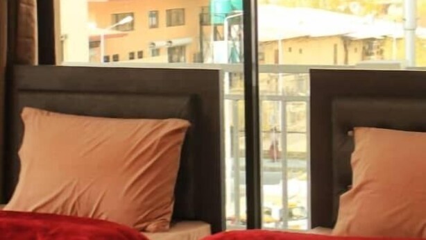 Habitación de hotel con dos camas, ventanas amplias y vistas a edificios.