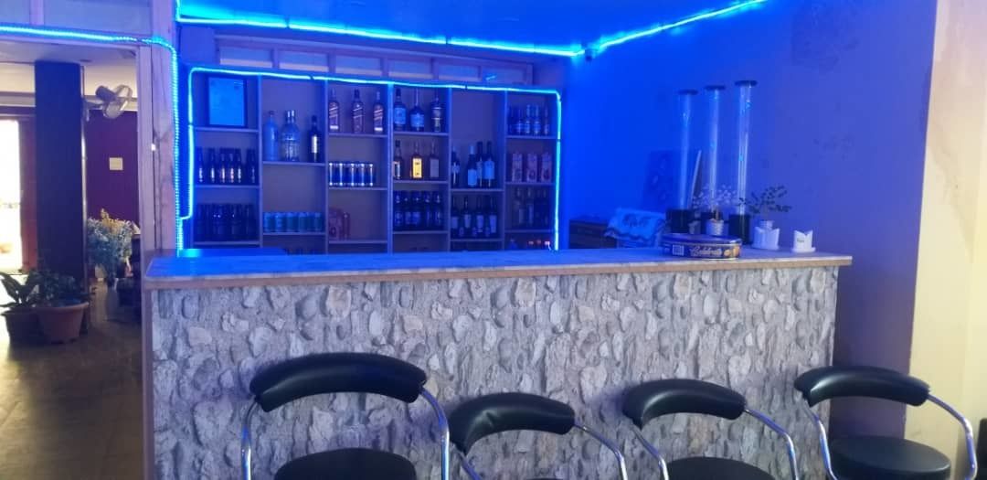A bar area with a stone counter, shelves of bottles, and bar stools.