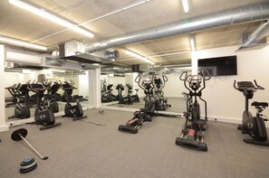 A gym with various exercise equipment, including treadmills, stationary bikes, and weight machines. - Leeds Urban Square Apartments (Leeds)
