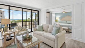 Une pièce spacieuse dotée d’une grande porte-fenêtre coulissante donnant sur un balcon avec vue sur l’océan. On y trouve un lit avec une tête de lit, un canapé et une table basse agrémentée d’objets décoratifs.