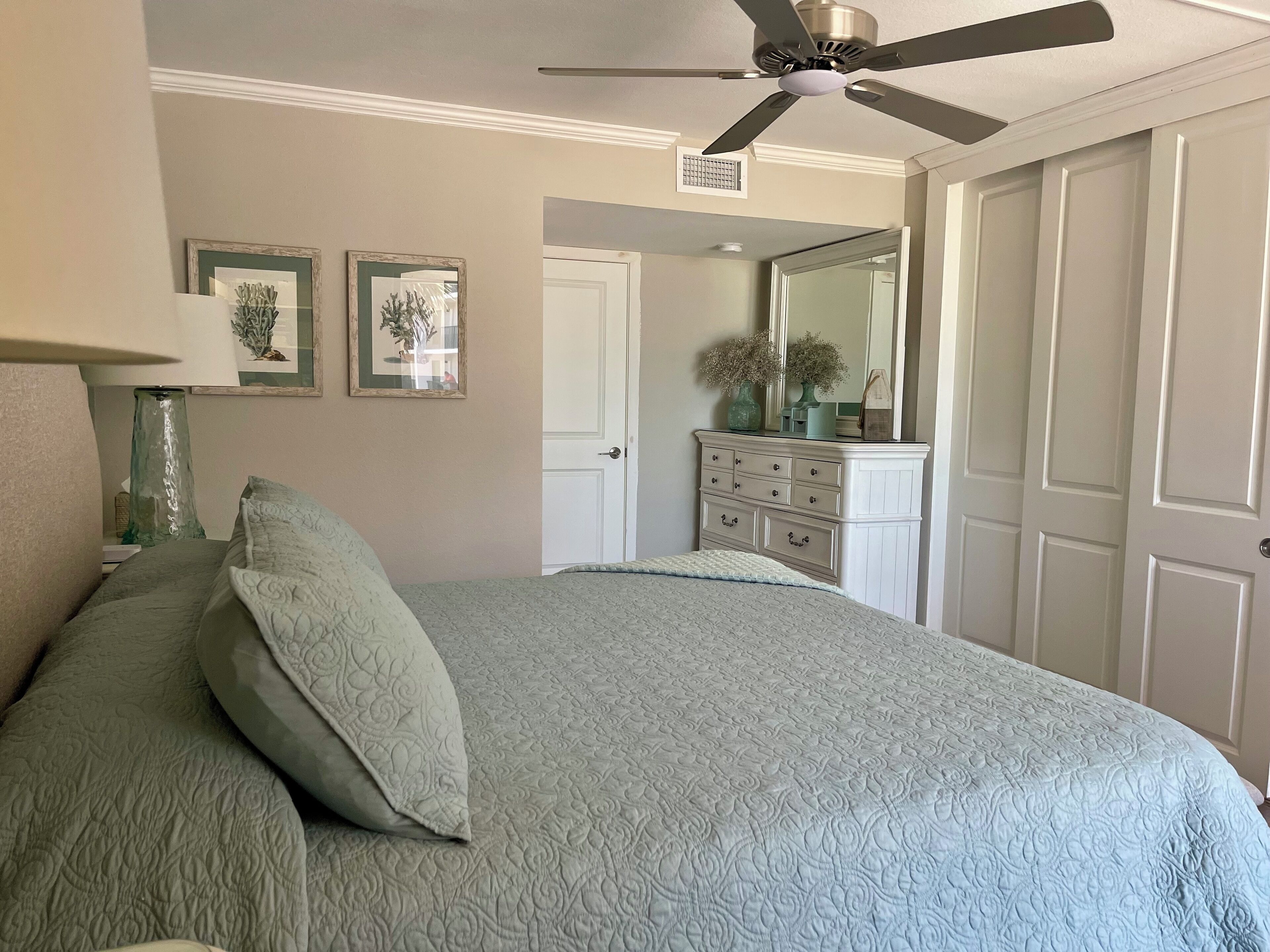A bedroom with a bed, a dresser, a mirror, and a ceiling fan.