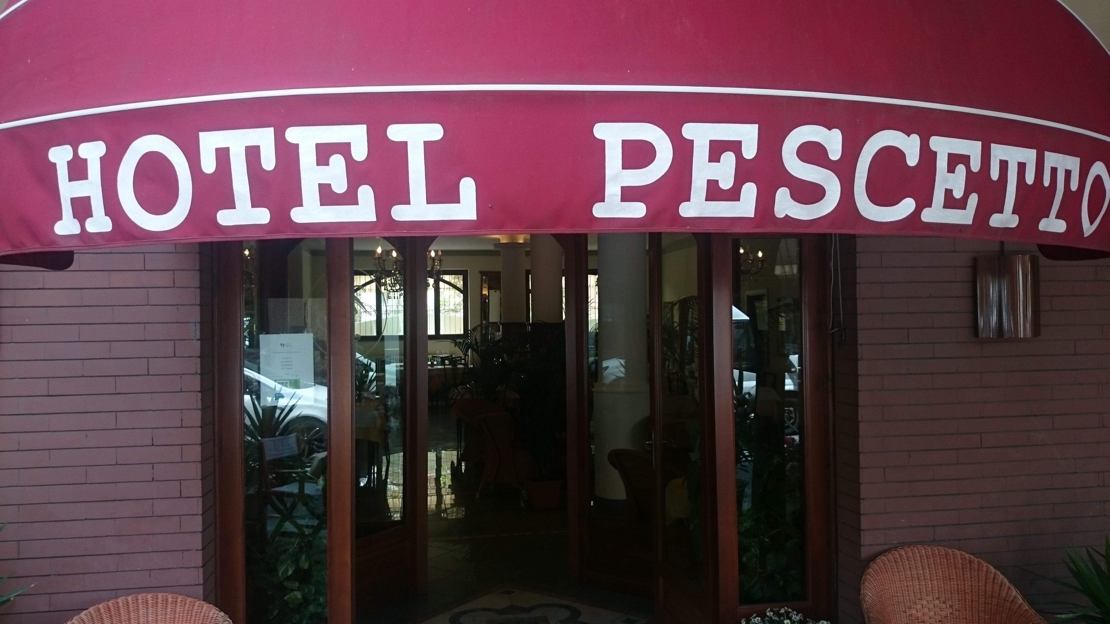L’entrée de l’hôtel Pescetto, avec son auvent bordeaux et ses portes en verre.