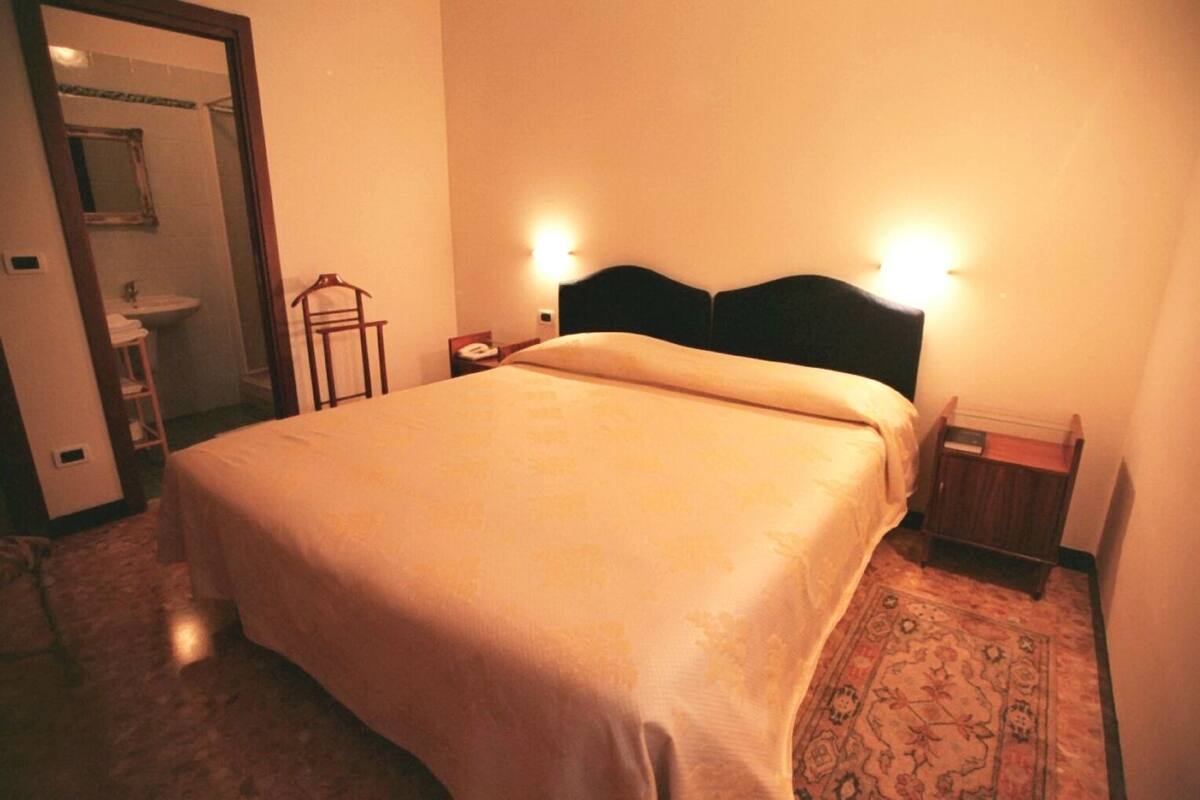 A hotel room with a bed, a nightstand, a bedside table, a mirror, and a bathroom visible through an open door.