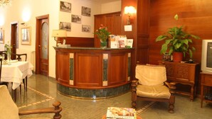 A reception area with a wooden reception desk, a chair, a television, and a potted plant. - Hotel Pescetto (Albenga)