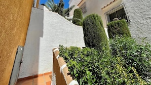 A narrow alleyway with white walls and a tiled floor, leading to a building with a window and a door.