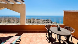 A terrace with a table and chairs, a view of the sea, and a tiled floor.