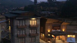 A traditional building with multiple balconies, a staircase leading to a covered entrance, and a small outdoor seating area. - Spirit of Bhutan Resort (Paro)