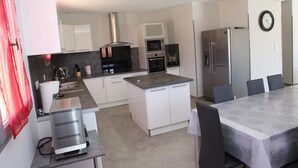 Una cocina moderna con armarios blancos, electrodomésticos de acero inoxidable, una isla central y un comedor con mesa y sillas.