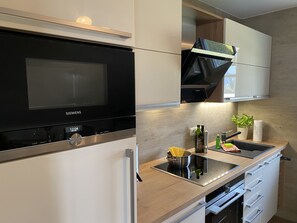 Una cocina moderna con microondas, estufa y horno integrados. Hay un lavamanos con grifo, una encimera con una planta y algunos utensilios de cocina.