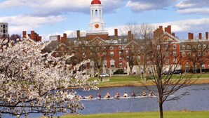 A historic building with a prominent clock tower, a river with rowers, and blooming trees. - MODERN Spacious 4bed 2bath HARVARD MIT BOS Cambridge Somerville walk everywhere! (Somerville)