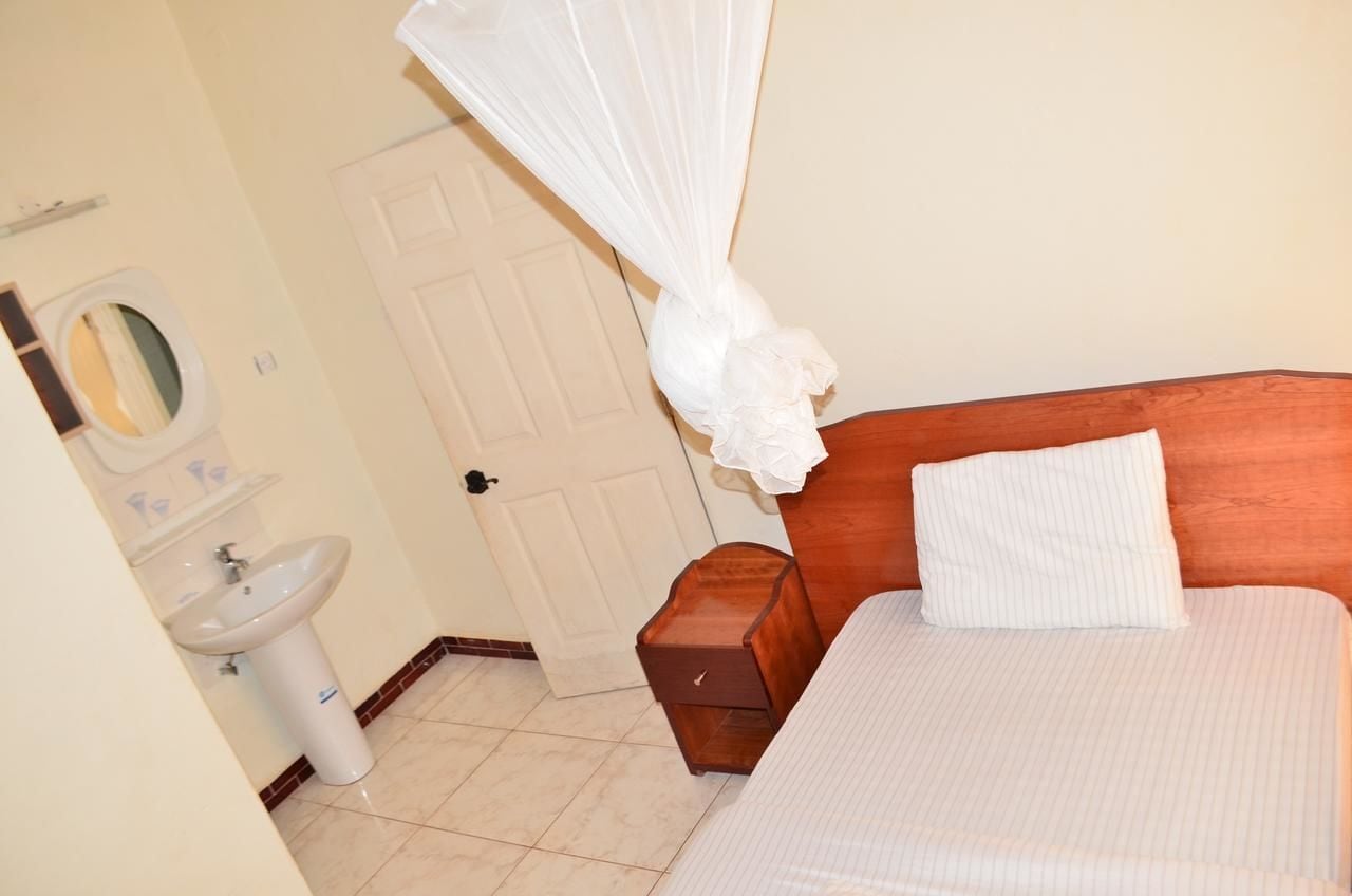 A bedroom with a wooden headboard, a white bedspread, a bedside table, and a white canopy over the bed.
