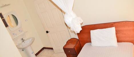 A bedroom with a wooden headboard, a white bedspread, a bedside table, and a white canopy over the bed.