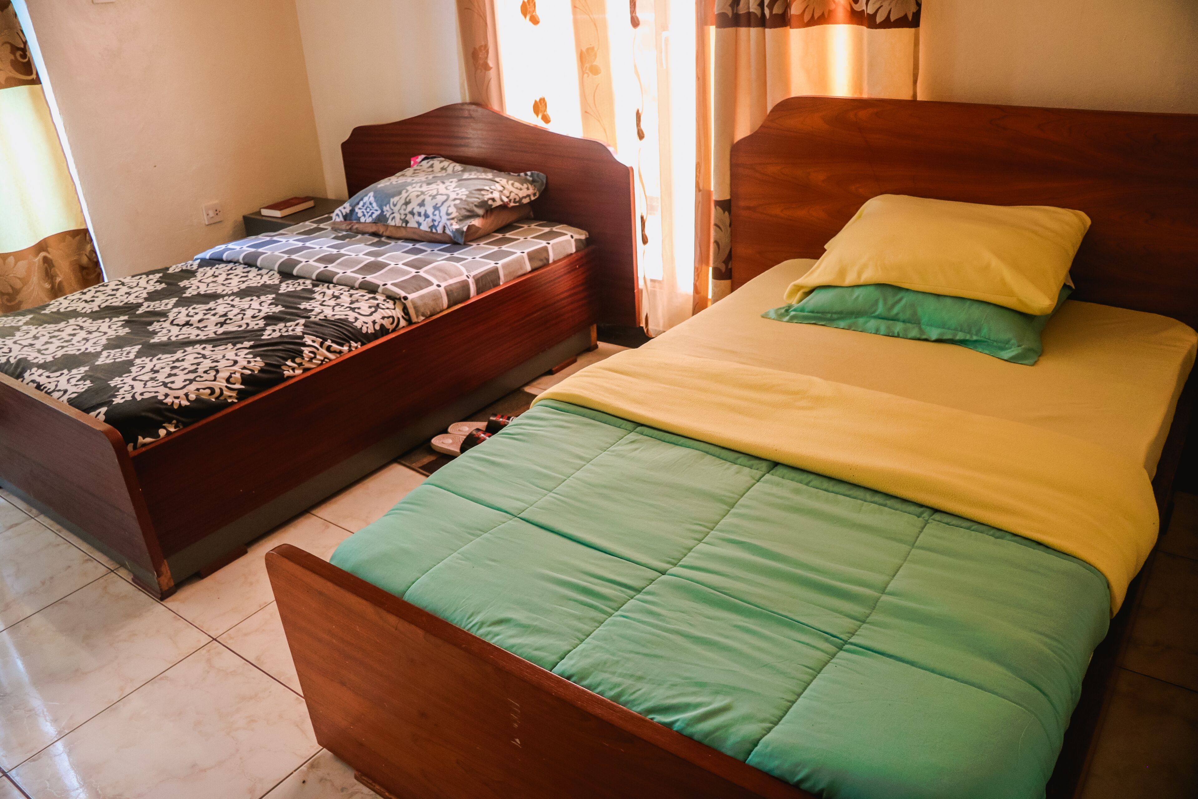 A bedroom with two beds, one with a patterned bedspread and the other with a solid green bedspread.