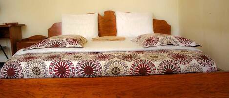 A bed with a wooden headboard, white and patterned bedding, and a wooden nightstand with a lamp.