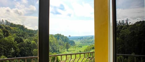 A balcony with a view of a lush green landscape and a clear sky.