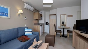 Un salon moderne comprenant un canapé, un téléviseur, un coin repas avec une table et des chaises, un coin cuisine avec un évier et des placards, et un climatiseur fixé au plafond.
