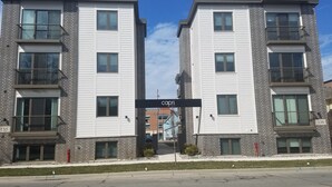A modern apartment building with a brick facade, multiple balconies, and a clear sky.