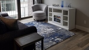 A living room with a sofa, a TV mounted on the wall, a white cabinet, and a large window with a view of a building.