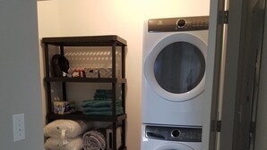 A laundry room with a washing machine and a shelving unit containing folded clothes and storage boxes.