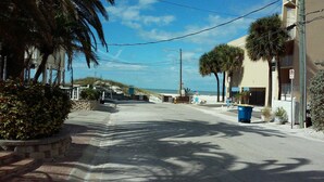 A coastal street with a clear view of the beach, a blue trash bin, and a no parking sign.