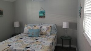 A bedroom with a bed, two bedside lamps, a wall-mounted sign, and a window with blinds.