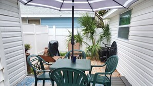 A patio with a table and chairs, a grill, and potted plants.