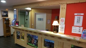 A reception desk with informational posters, a lamp, and a red wall with a 'METEO' sign.