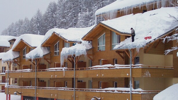 A multi-story wooden building with snow-covered roofs and icicles.