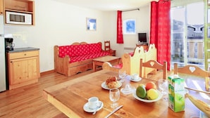 A cozy room with a wooden dining table set for breakfast, a red sofa, and a kitchen area with a microwave.