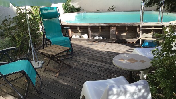 A wooden deck with a pool, a blue lounge chair, a white table, and an umbrella. - Charming apartment with private pool and secure parking (Nîmes)