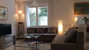 A living room with a sofa, a glass coffee table, a television, and a window with curtains. - Charming apartment with private pool and secure parking (Nîmes)