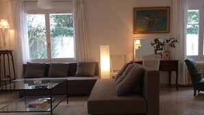 A living room with a sofa, a glass coffee table, a chair, a lamp, and a painting on the wall. - Charming apartment with private pool and secure parking (Nîmes)