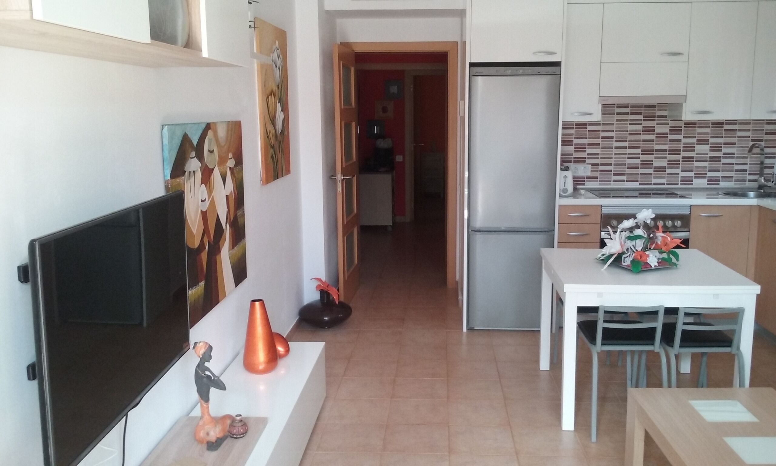 A modern kitchen with white cabinets, a built-in oven, and a dining area with a table and chairs.