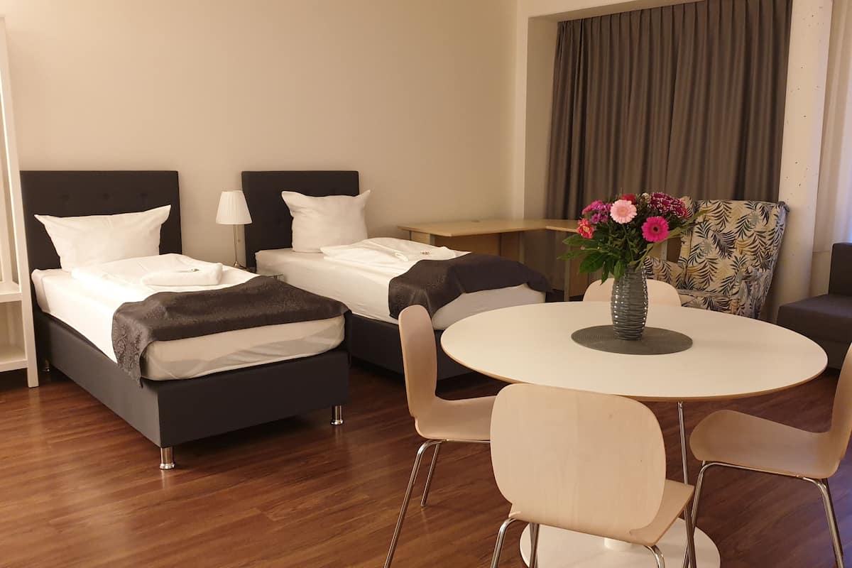 Une chambre d’hôtel comprenant un lit, un canapé, une table à manger avec des chaises et un vase avec des fleurs.