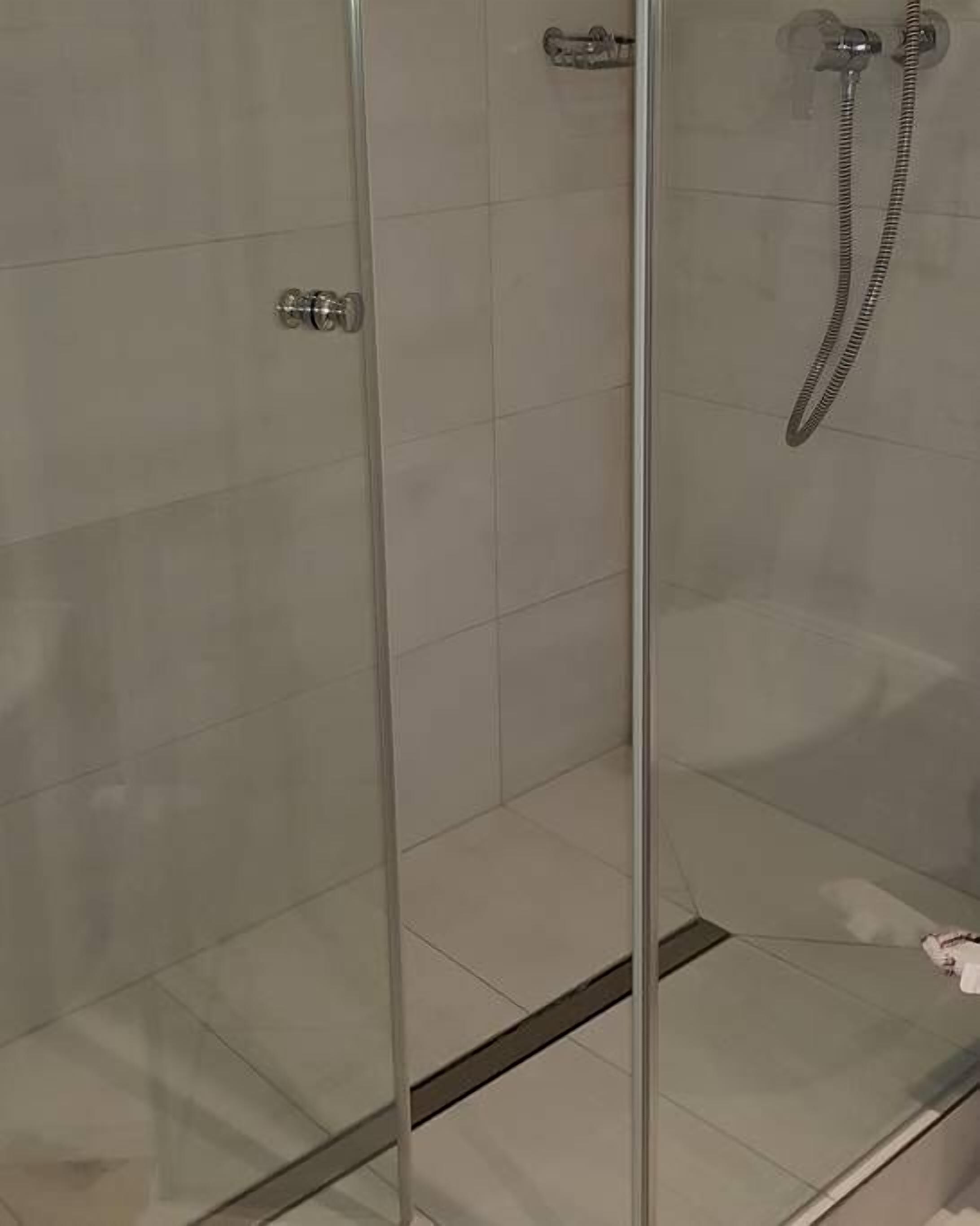 Un área de ducha con paredes de azulejos y ducha de metal, completamente cerrada por vidrio.