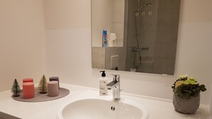 A bathroom with a white sink, a mirror, a shower, and a small potted plant. - Apart- Hotel Kick (Sinsheim)