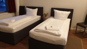 Two single beds with white linens and pillows, a small table with a vase of flowers, and a chair. - Apart- Hotel Kick (Sinsheim)