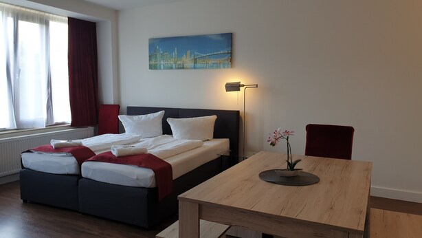 A hotel room with a bed, a table, a chair, a painting, and a lamp. - Apart- Hotel Kick (Sinsheim)