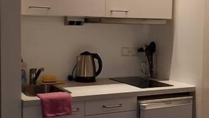 A compact kitchen with white cabinets, a countertop, a kettle, and a dishwasher. - Apart- Hotel Kick (Sinsheim)