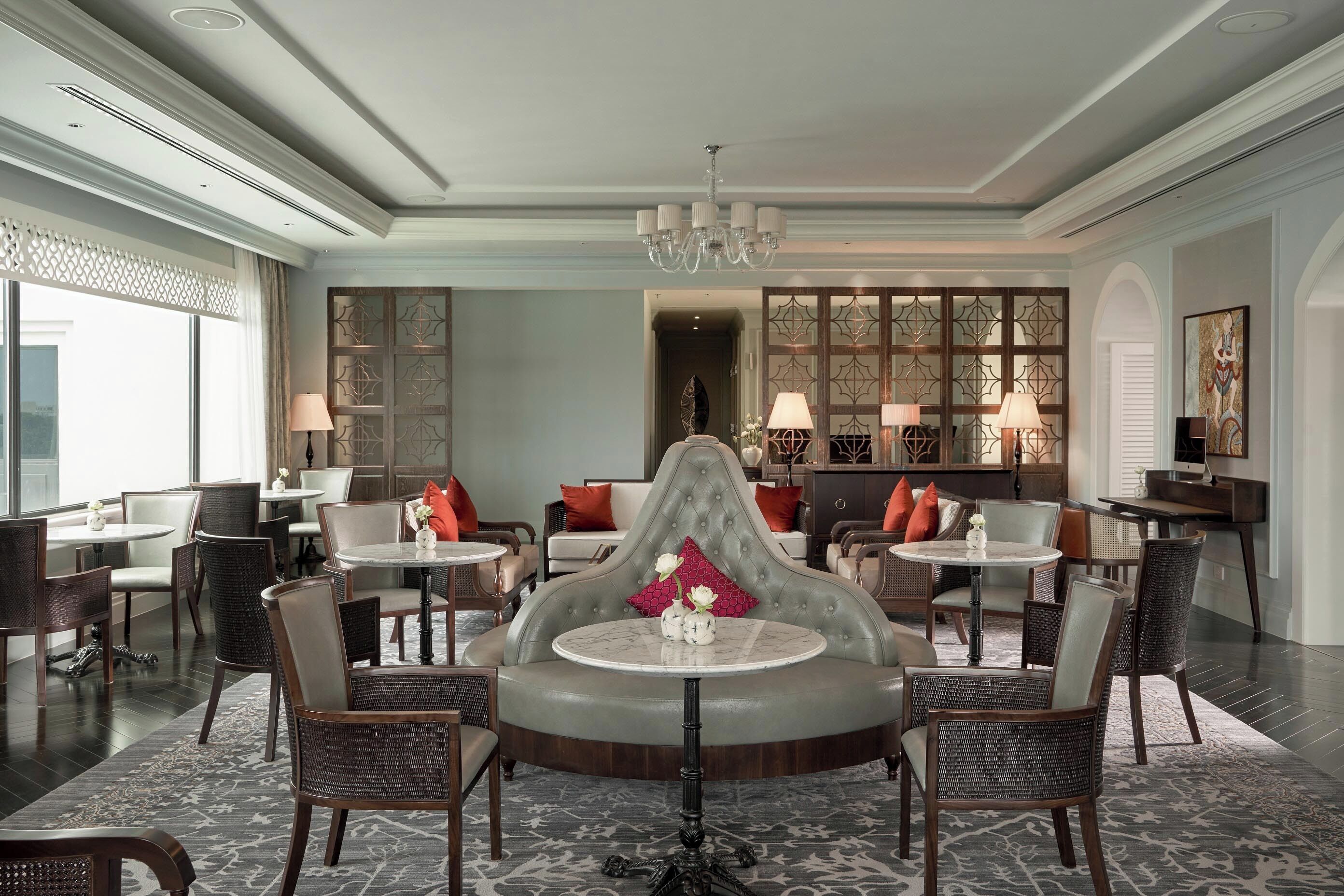 A spacious lobby with a central seating area, multiple tables, and chairs, and a decorative partition with a chandelier above.