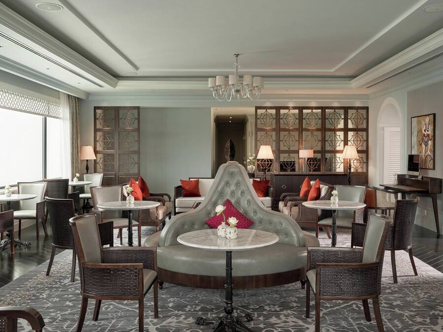 A spacious lobby with a central seating area, multiple tables, and chairs, and a decorative partition with a chandelier above.