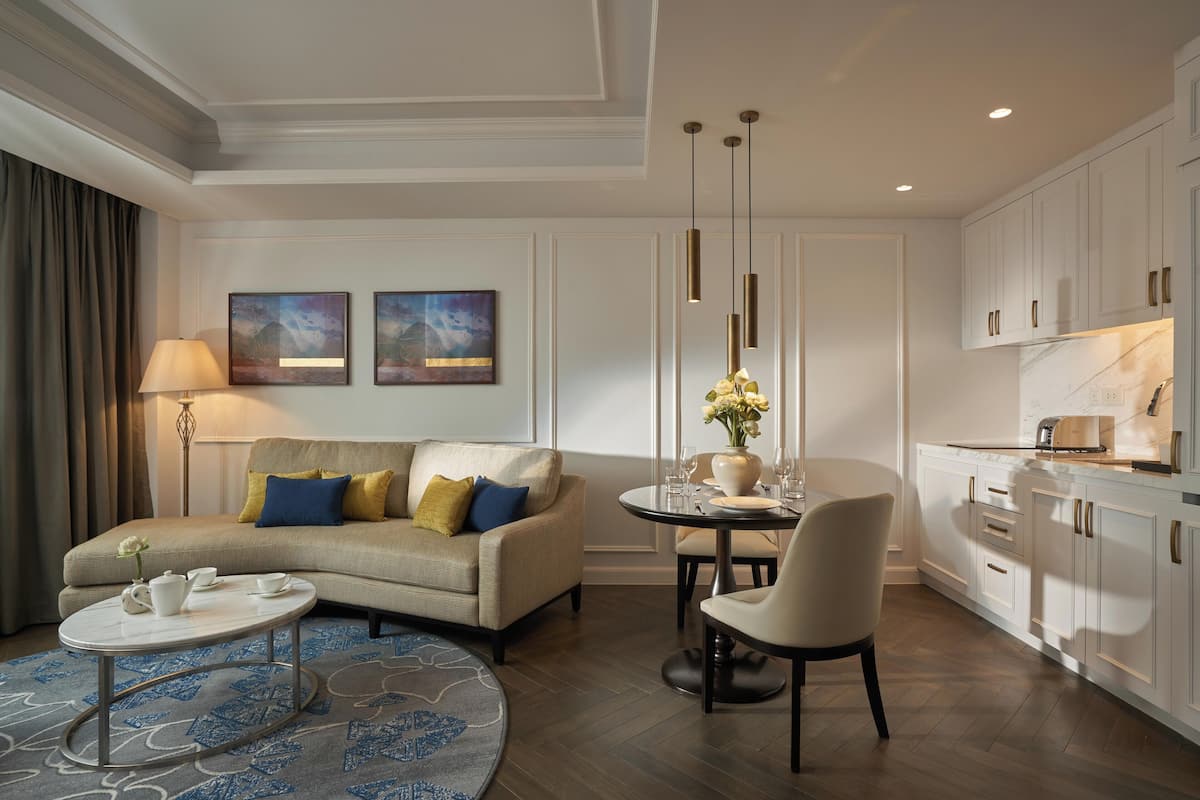 A modern living room with a sofa, coffee table, and dining area. There is a kitchen with white cabinets and a marble countertop.