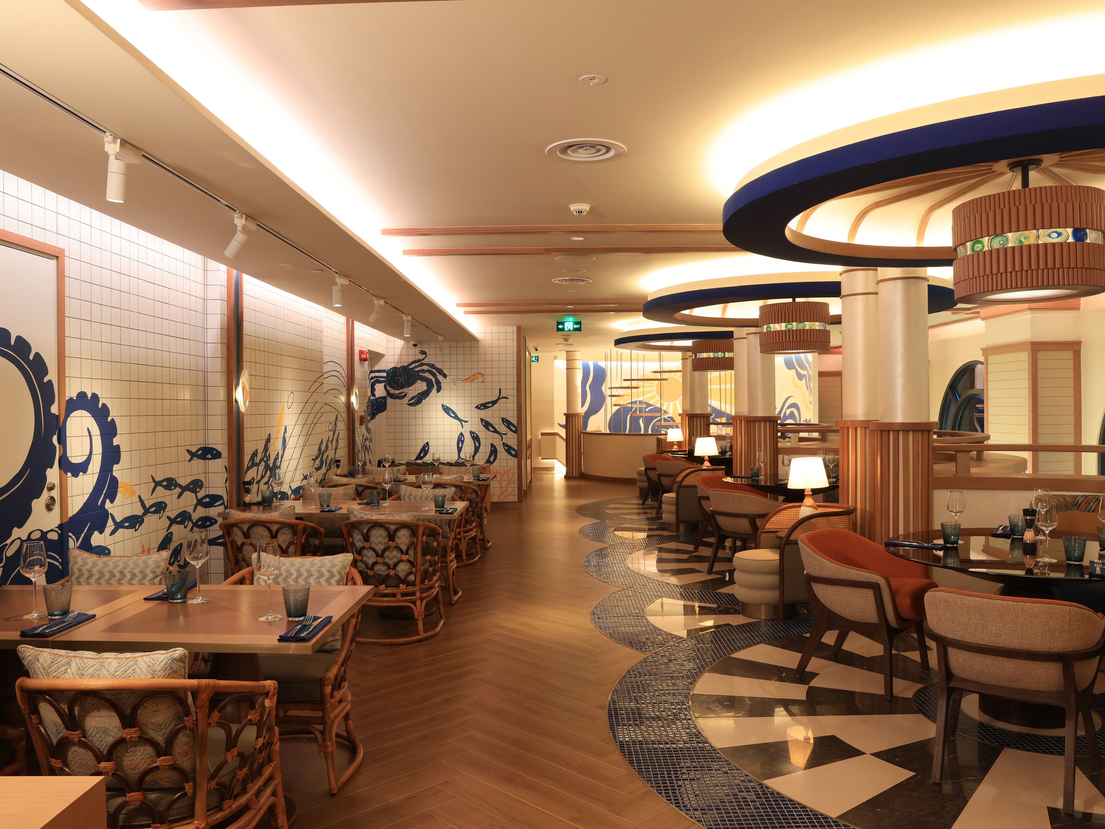 A restaurant with wooden flooring, tiled walls with seafood designs, and a variety of seating arrangements including tables and chairs.
